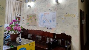 A room with a wooden bench, a desk with a computer, a vase of flowers, and a wall with clocks and handwritten notes. - Galaxy Motel Hpa An (Hpa-An)
