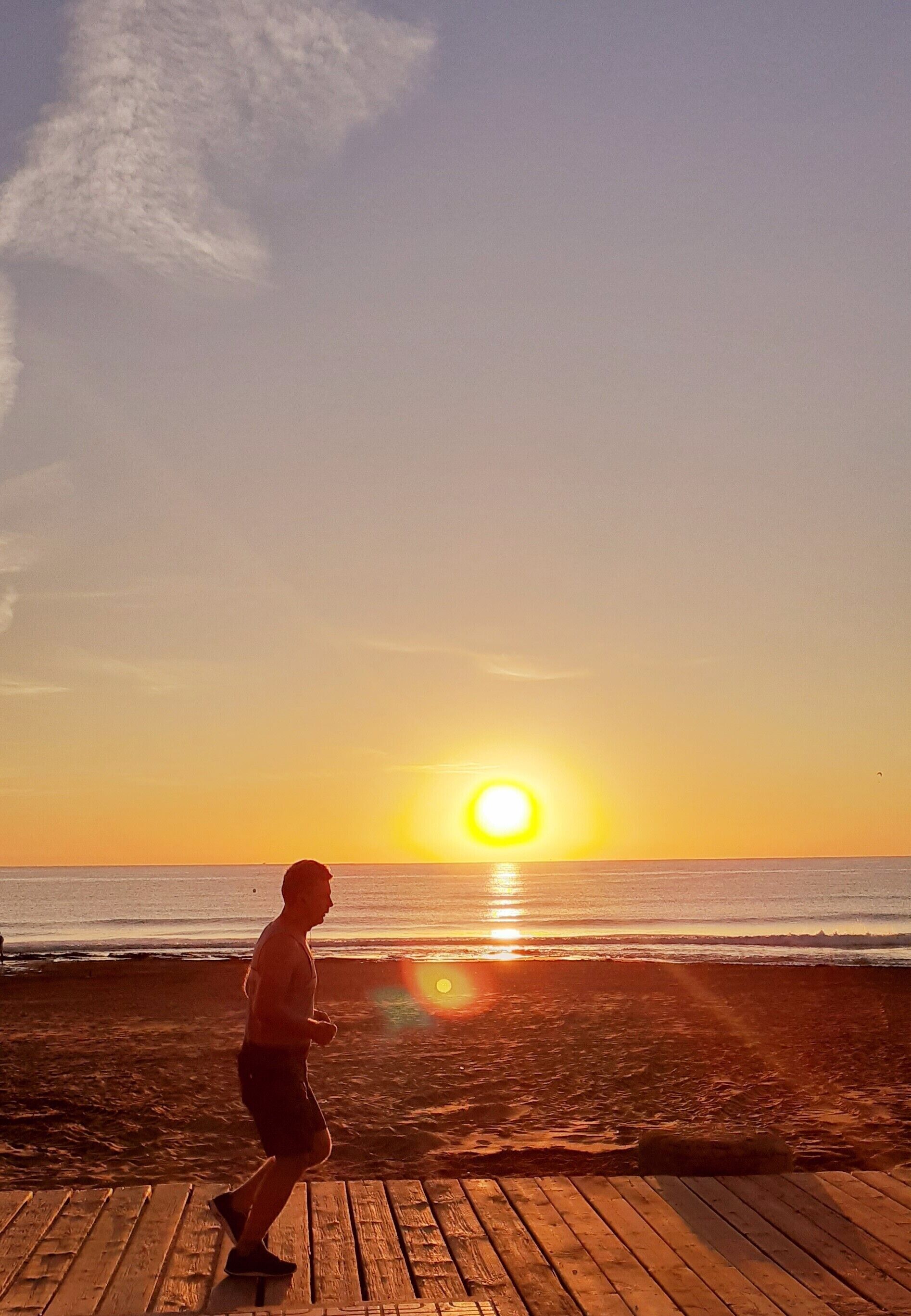 A wooden deck leading to a beach with a sunset in the background.