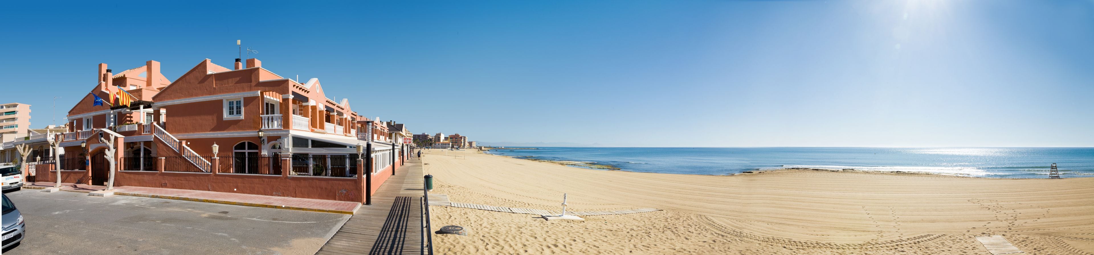 A beachfront hotel with a long boardwalk, ocean views, and a clear sky.