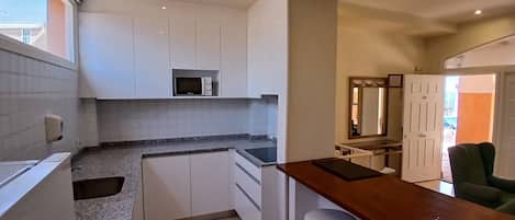 A compact kitchen with white cabinets, a microwave, a sink, and a bar area with stools.