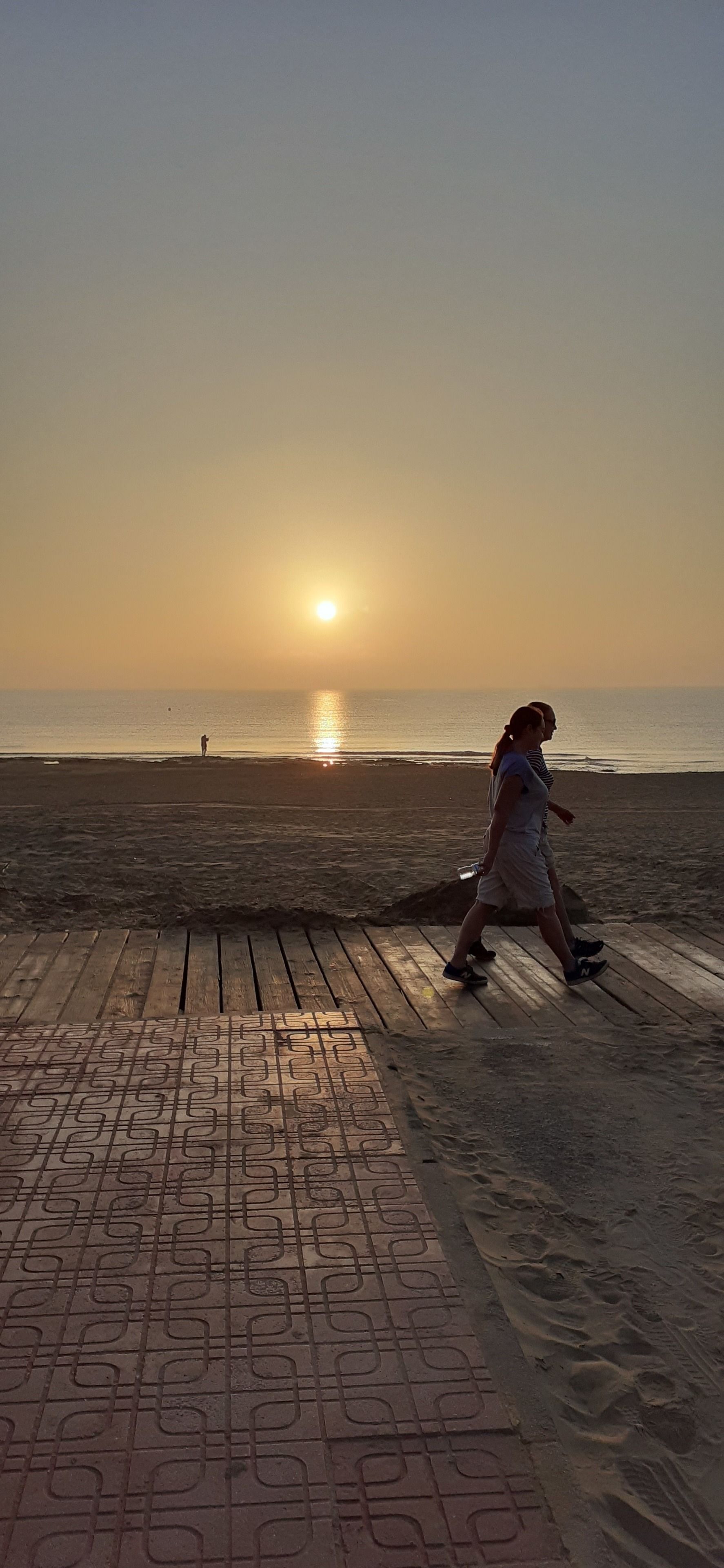 Une promenade en bois menant à une plage, avec un coucher de soleil en arrière-plan.