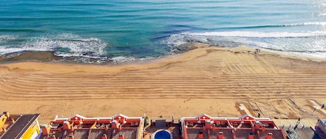 A beach view with a swimming pool and red-roofed buildings.