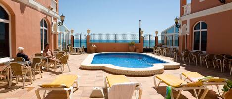 A poolside area with lounge chairs and a swimming pool, surrounded by buildings with balconies and windows.