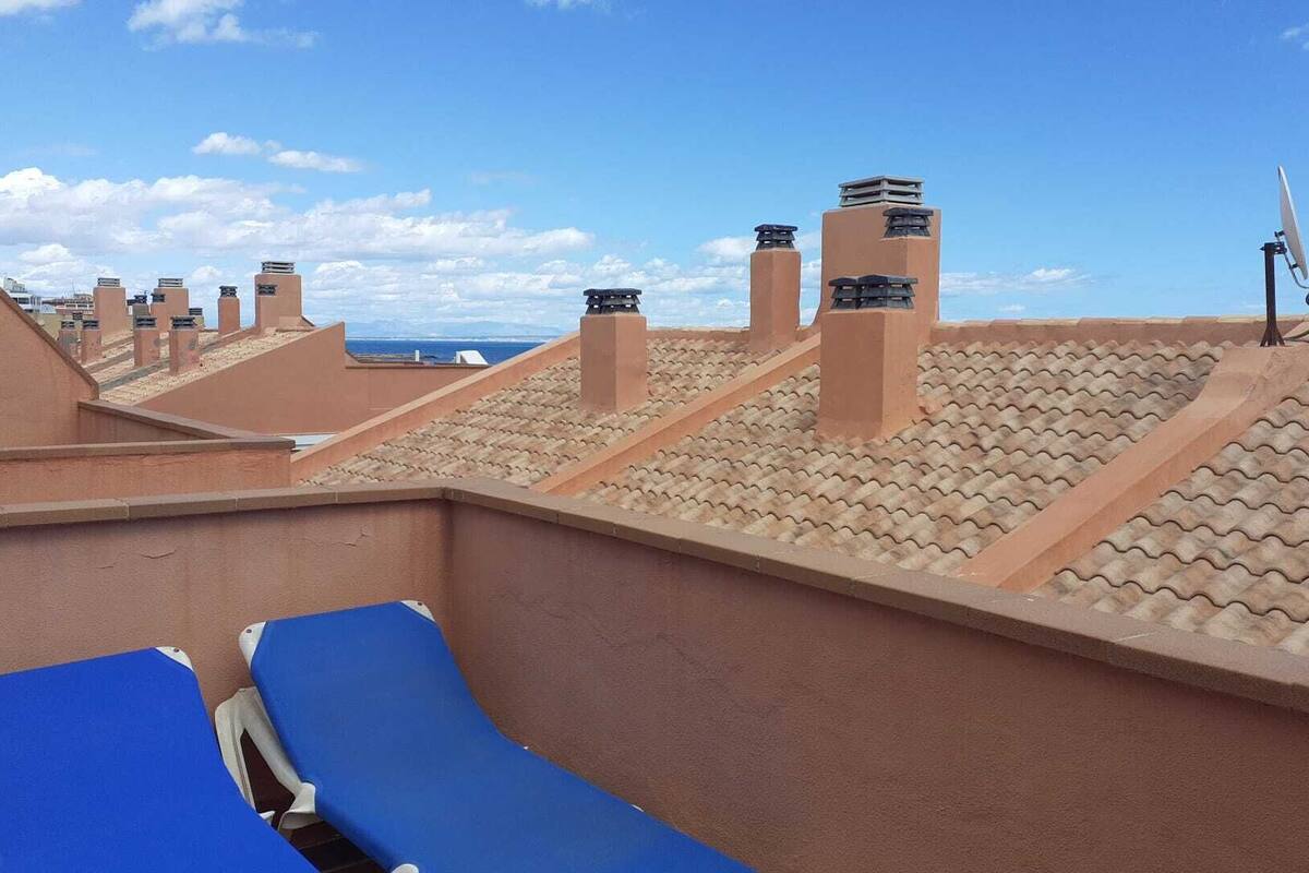 Une terrasse sur le toit, avec des fauteuils de jardin bleus, une antenne parabolique et une vue sur l’océan.