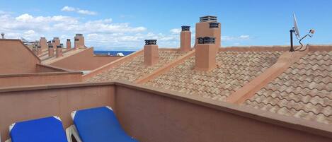 A rooftop terrace with blue lounge chairs, a satellite dish, and a view of the ocean.
