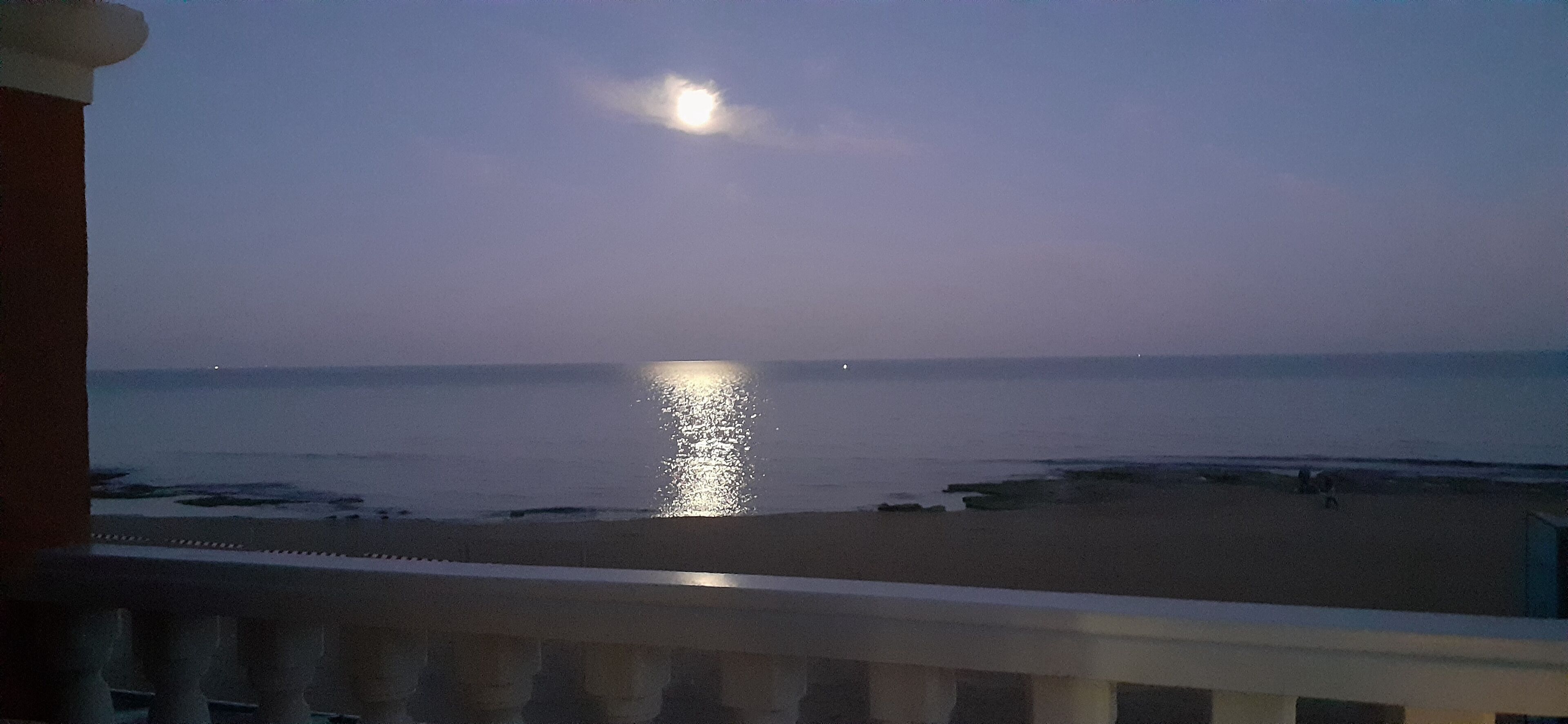 Un balcone con vista sul mare e il riflesso della luna sull'acqua.