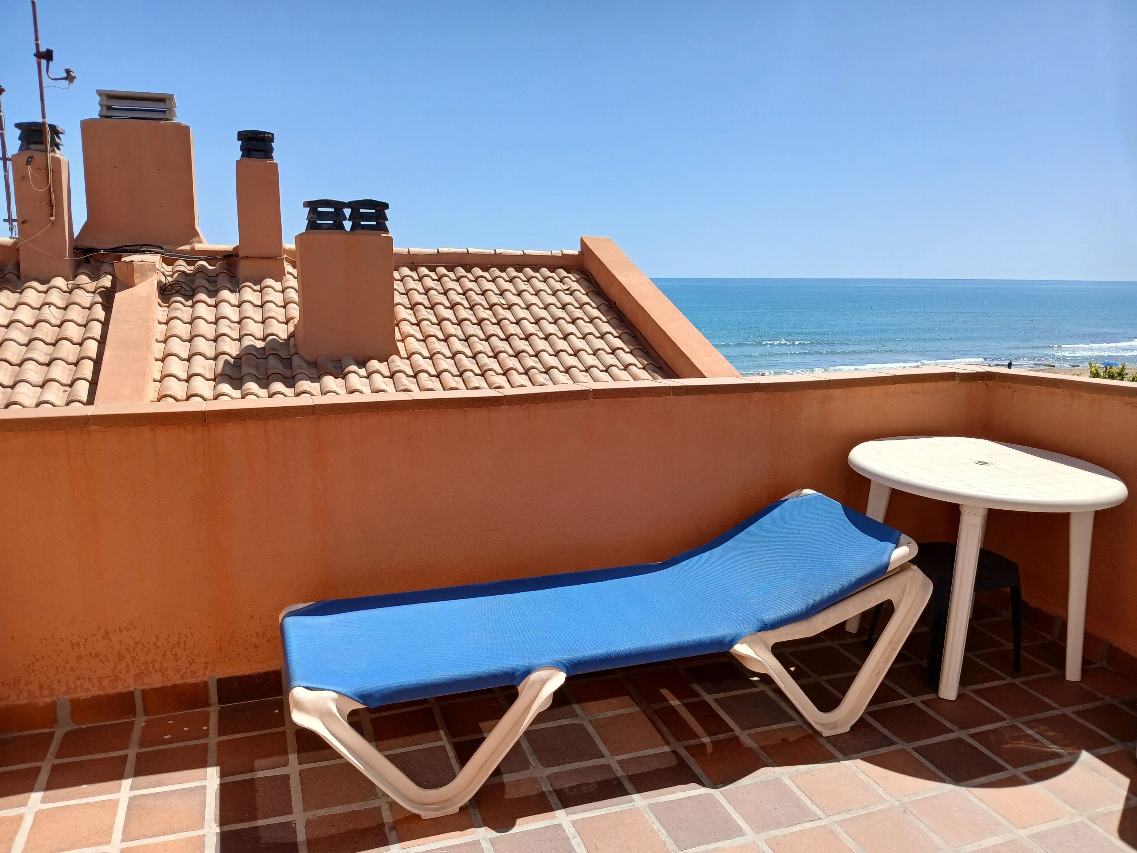 Un balcone con una poltrona blu e un tavolino, con vista sul mare.