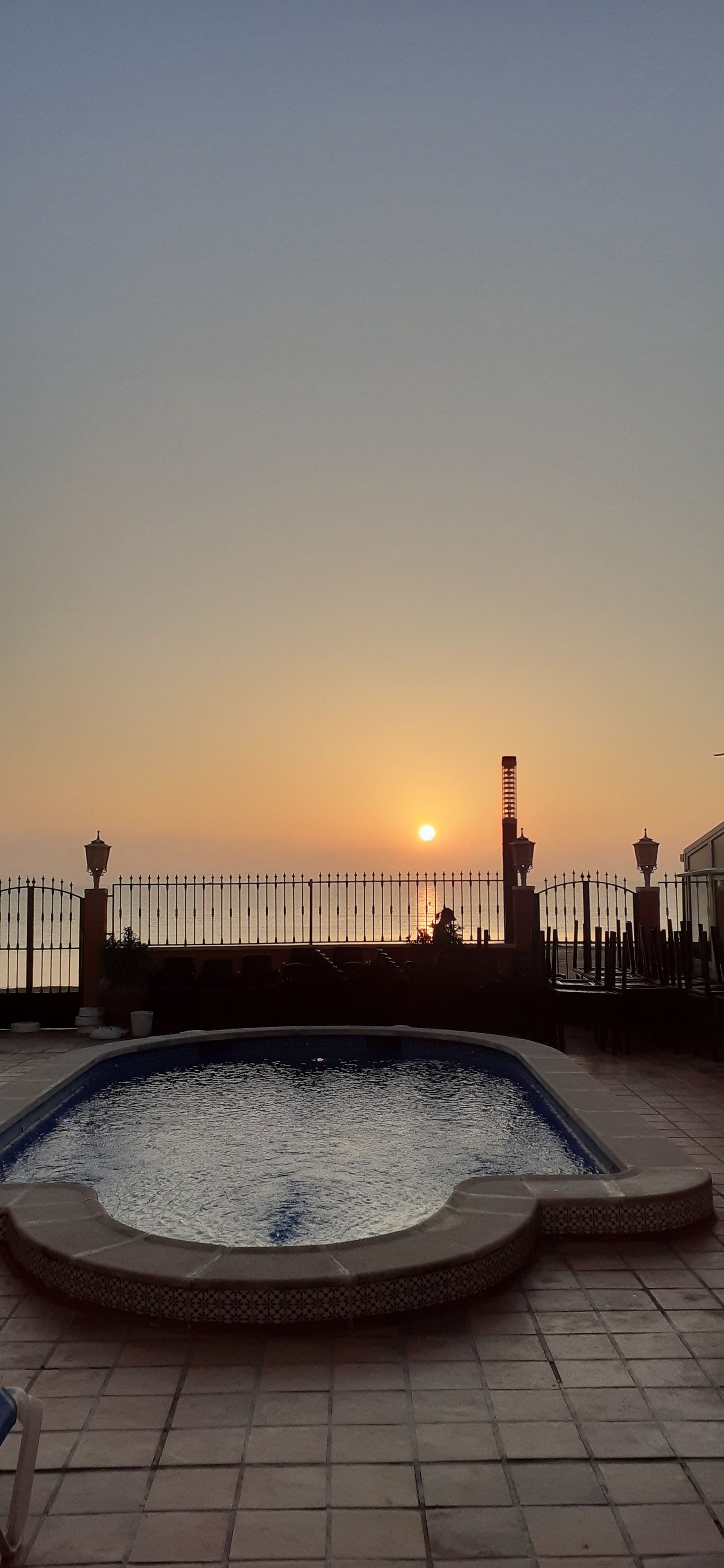 A rooftop pool with a view of the sunset over a city skyline.