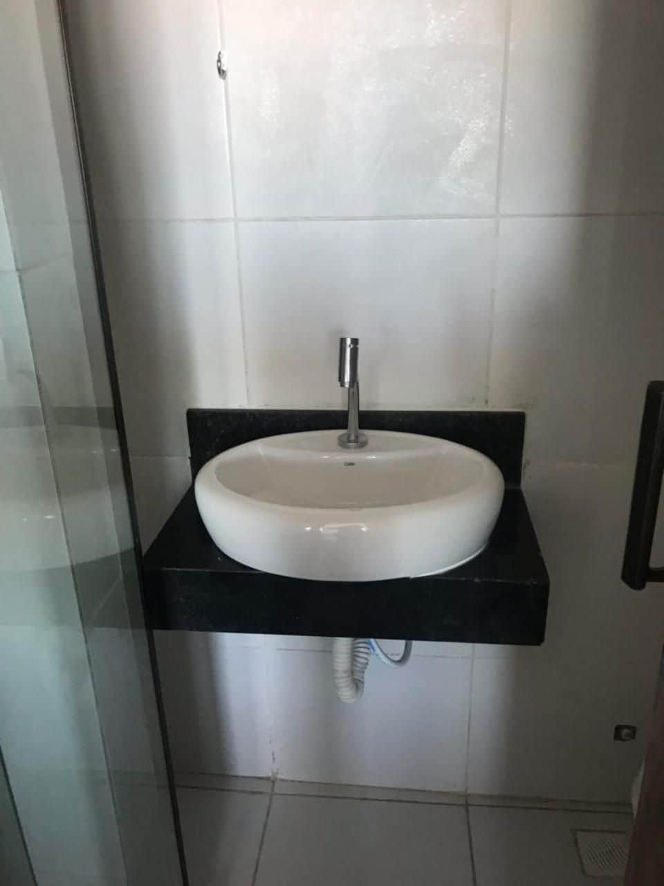 Une salle de bain avec un lavabo blanc posé sur un plan de toilette noir, une douche en verre et des murs carrelés.