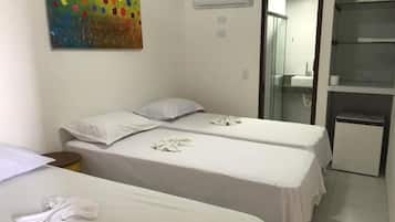 Quarto de hotel com duas camas de solteiro, uma mesinha, geladeira, ar-condicionado e um quadro colorido na parede.