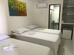 Une chambre d’hôtel avec deux lits simples, une petite table, un réfrigérateur, un appareil de climatisation et un tableau coloré accroché au mur.