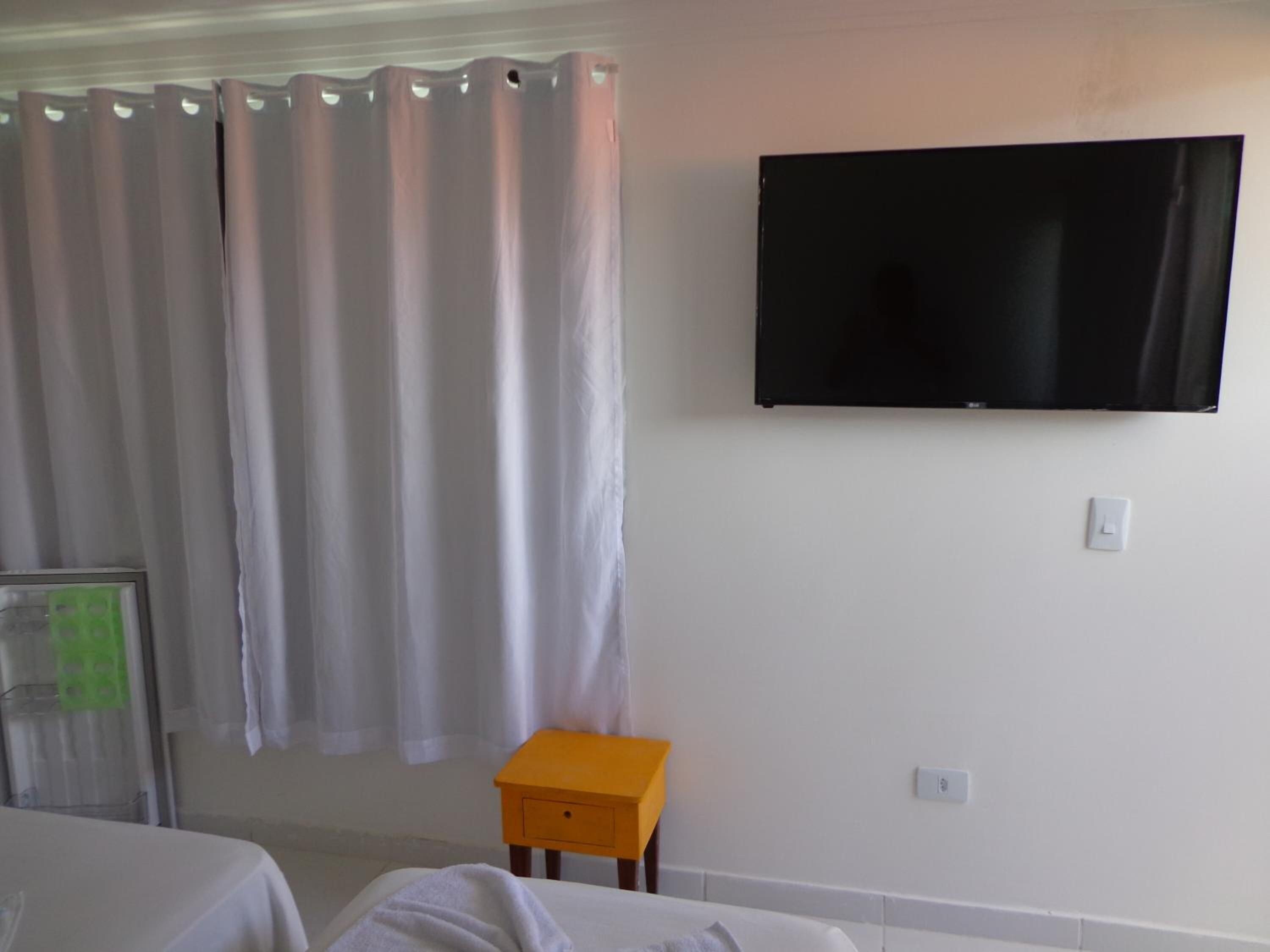 Una habitación de hotel con una cama, una mesita, un televisor montado en la pared y una cortina.