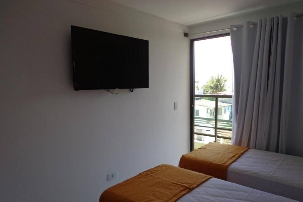 Habitació d'hotel amb dos llits, televisió de pantalla plana penjada a la paret i una finestra gran amb cortines.