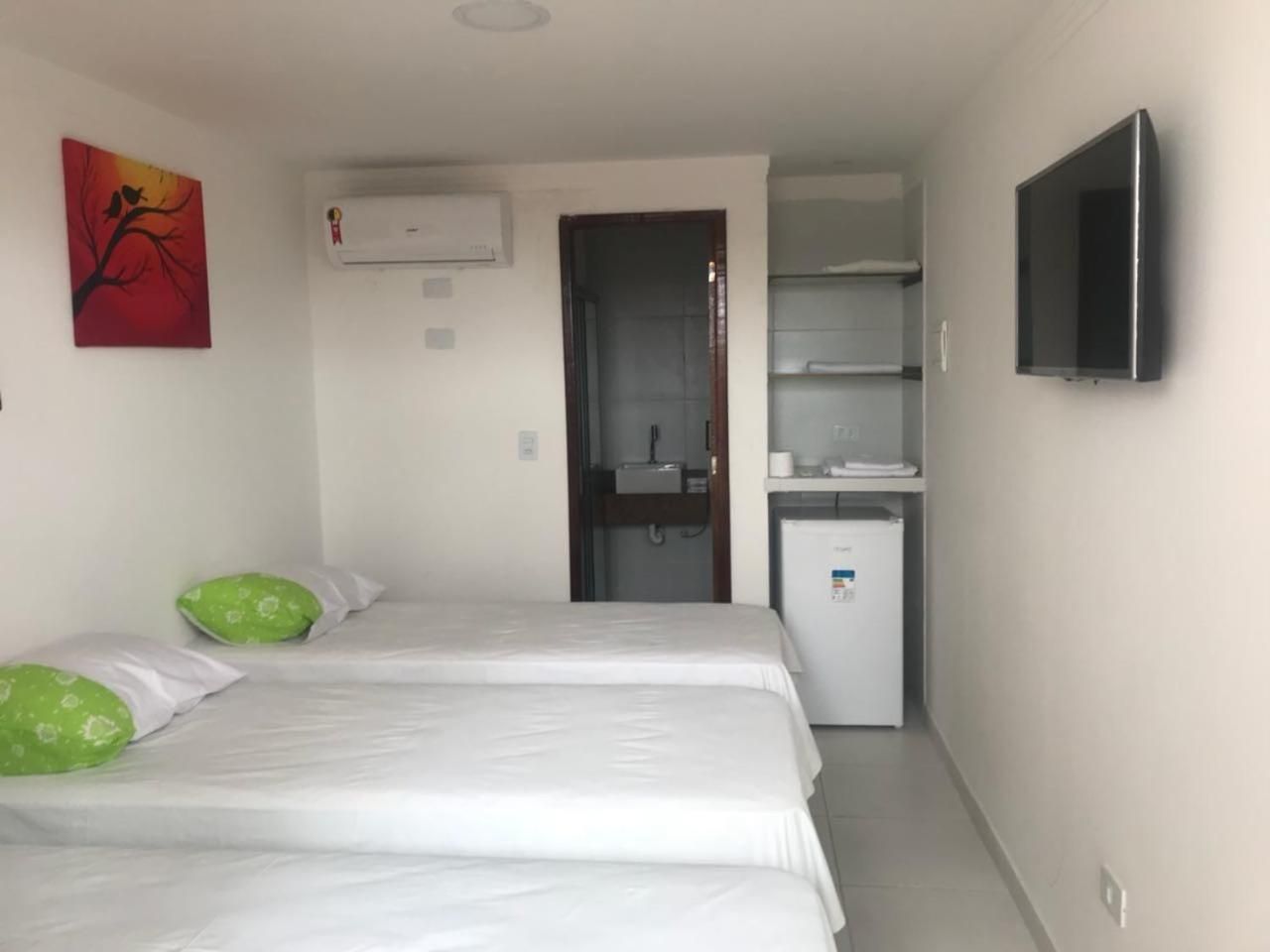 A hotel room with two beds, a small kitchenette, a TV, and a painting on the wall.