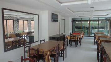 Uma sala de jantar com várias mesas e cadeiras, um espelho grande e uma televisão na parede.