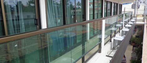A modern building with a glass balcony, outdoor seating area, and a view of the surrounding buildings.