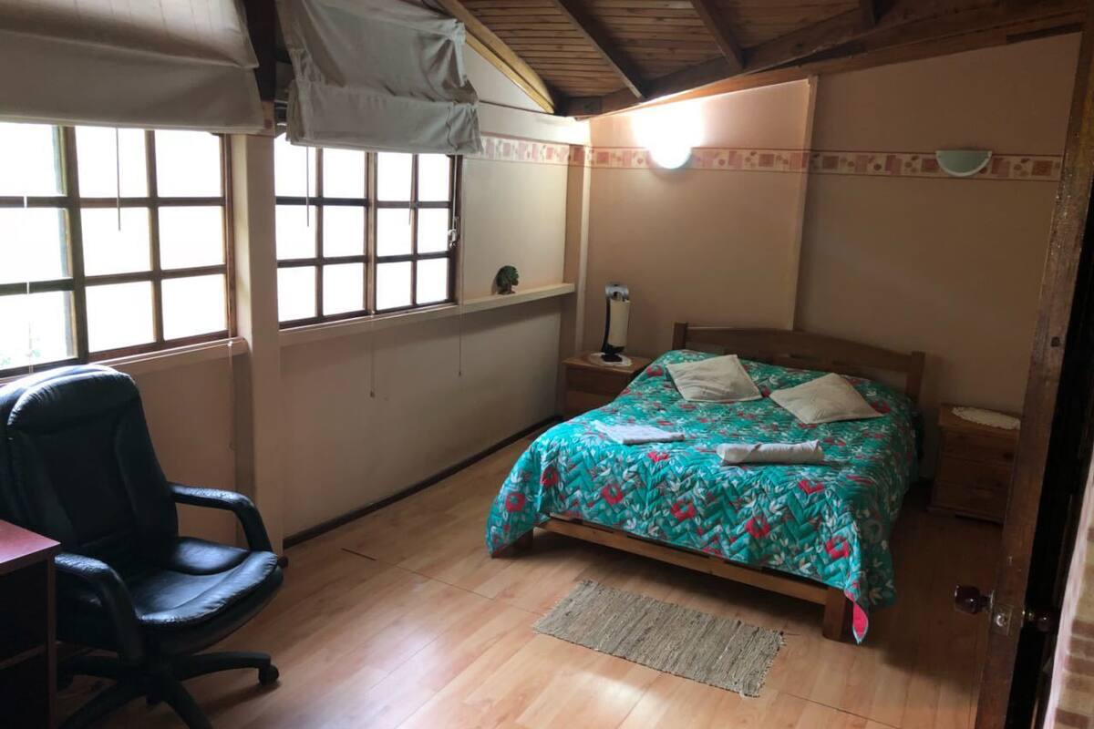 A bedroom with a bed, a chair, a nightstand, a lamp, and a window.