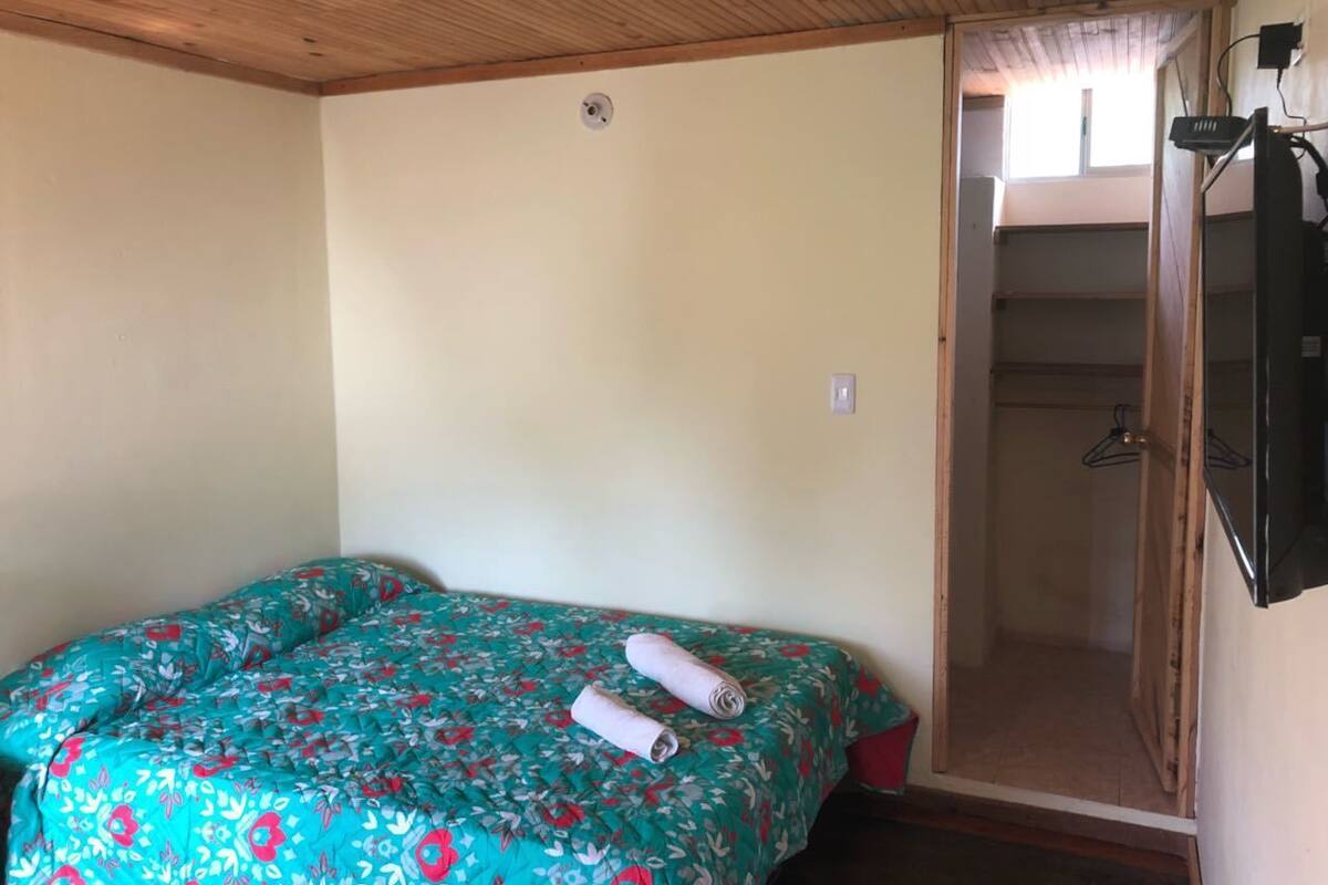 A room with a bed, a door leading to a bathroom, and a ceiling with wooden beams.