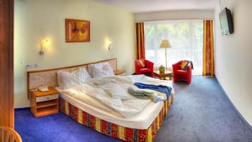 Una camera d'albergo con un letto, un comodino, una lampada e due poltrone.