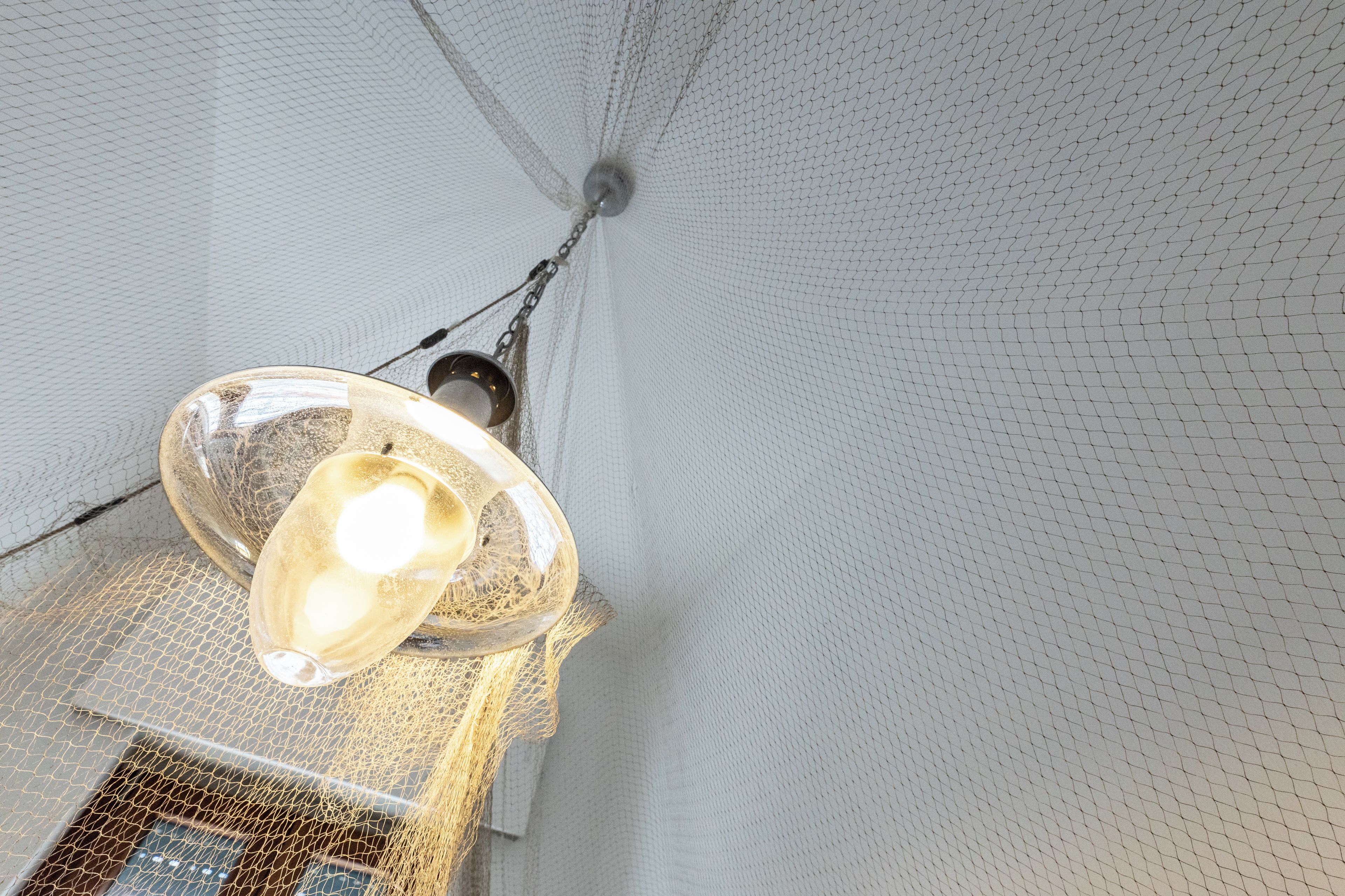 A room with a hanging light fixture and a netted ceiling.