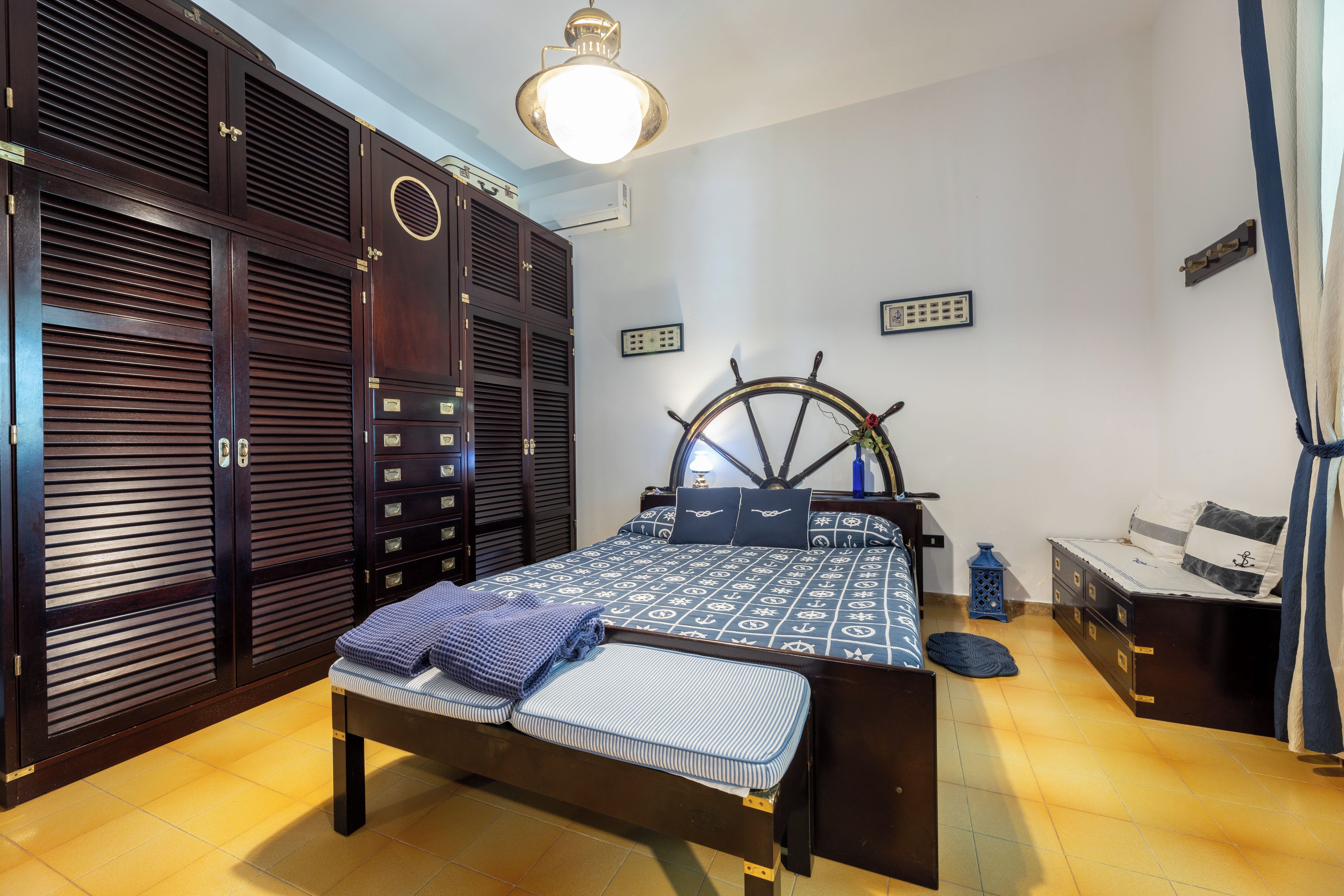A bedroom with a bed, wardrobe, and a ship's wheel decoration.