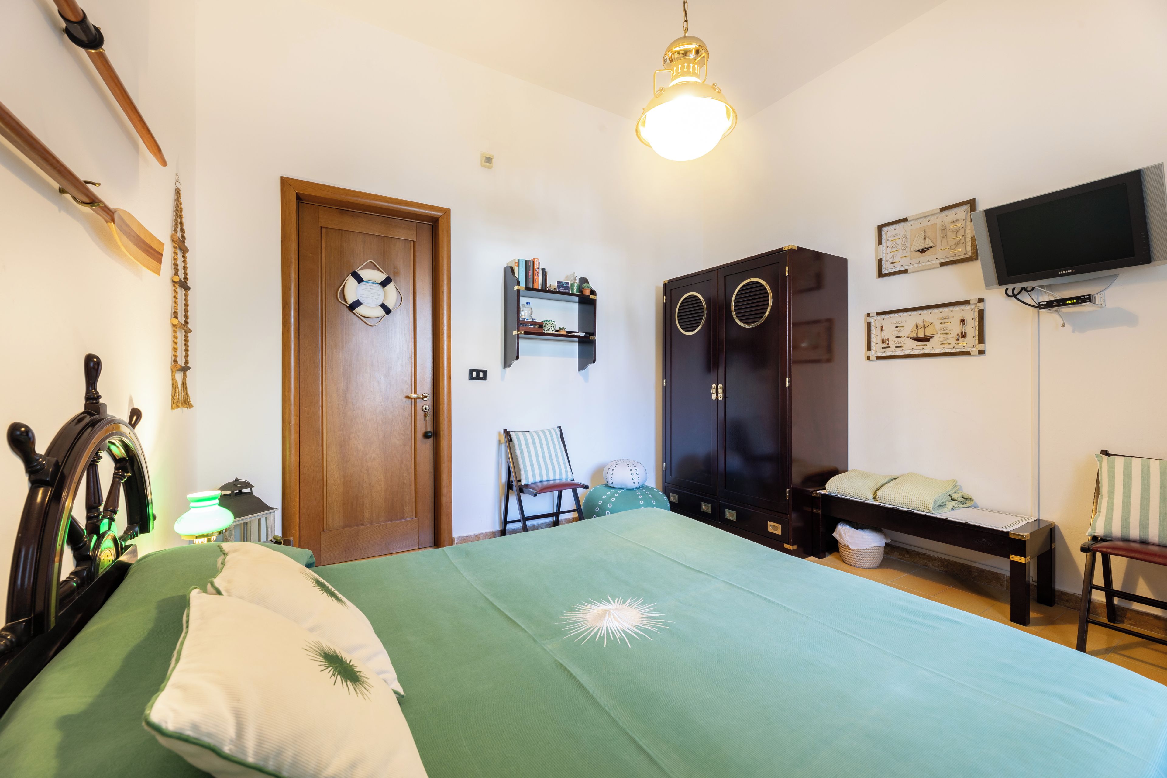 A bedroom with a bed, a wardrobe, a television, and a door with a life preserver.