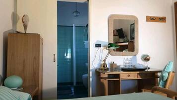Un dormitorio con cama, armario de madera, escritorio con espejo y baño a la vista a través de una puerta abierta.