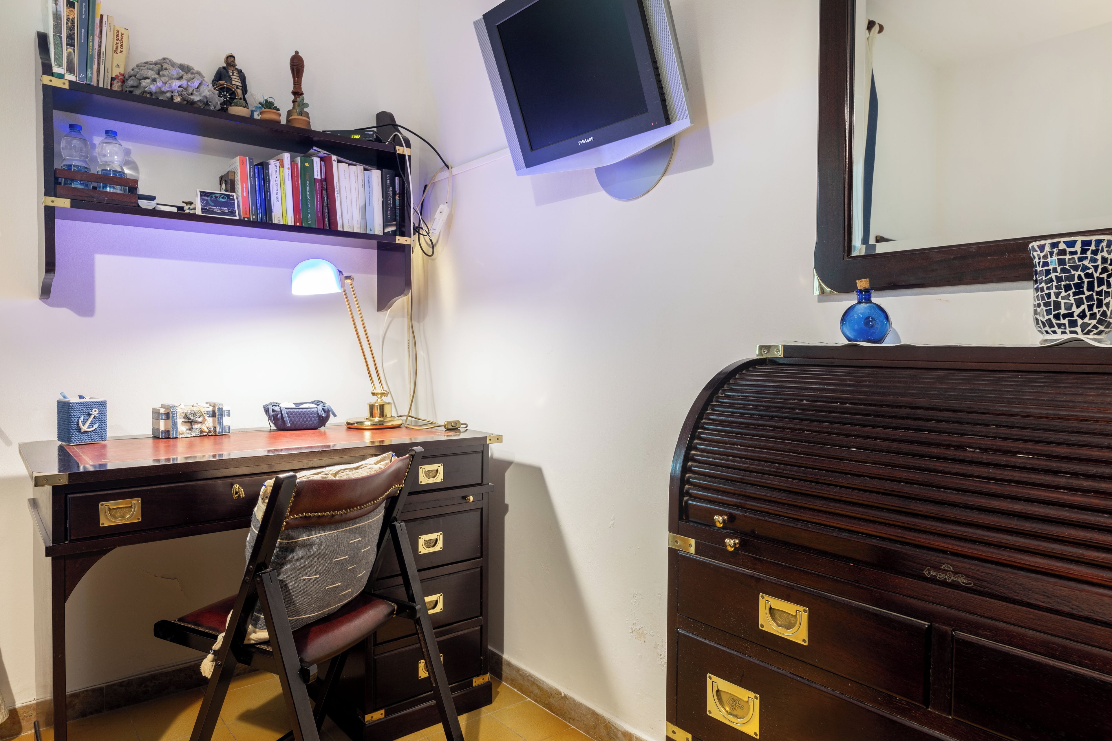 A study room with a desk, chair, bookshelf, lamp, and a large mirror.