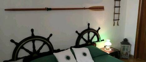 A bed with a green bedspread and two white pillows with black designs, a wooden headboard with a ship's wheel design, and two wooden oars hanging on the wall above the bed.