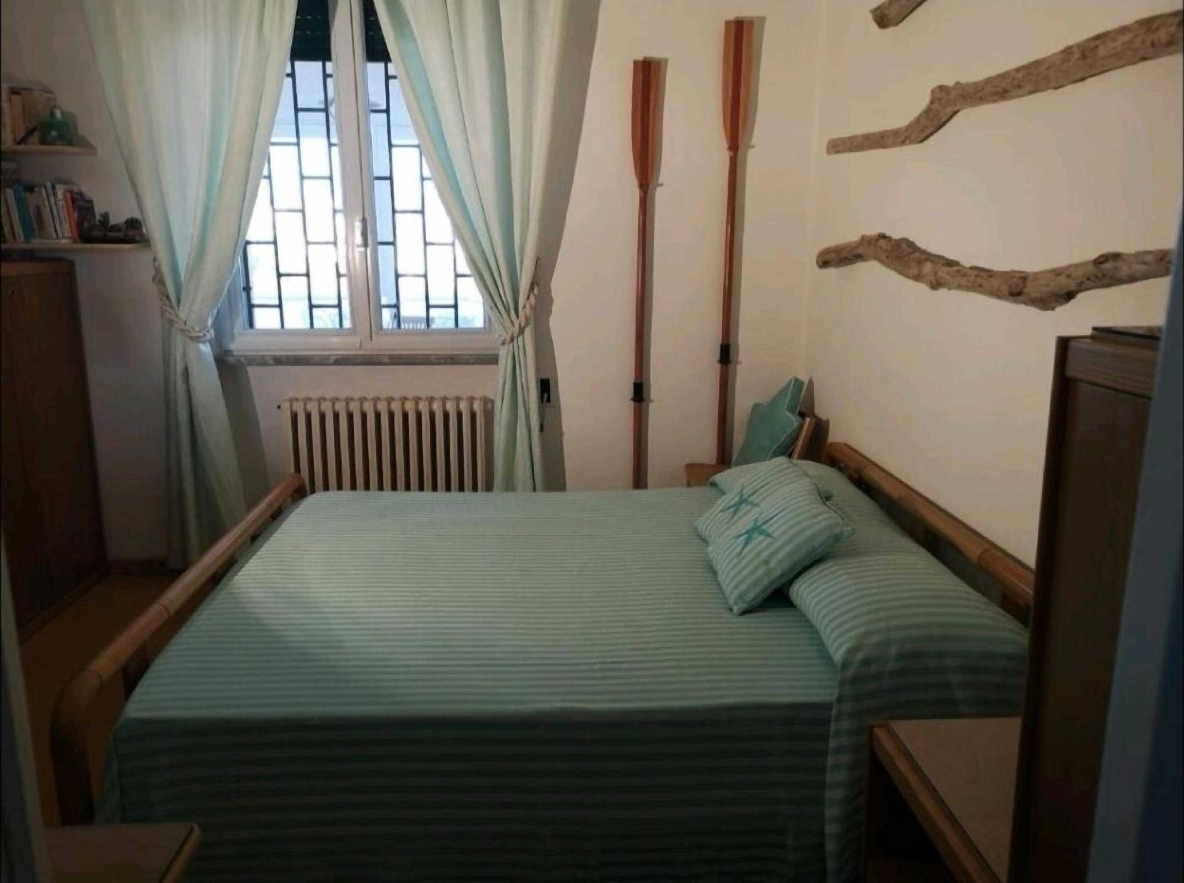 A bedroom with a bed, curtains, a radiator, and a window with bars.