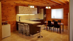 A modern kitchen with a central island, bar stools, a dining table with chairs, wooden walls, and a window with blinds. - Ekodom (Voropaiv)