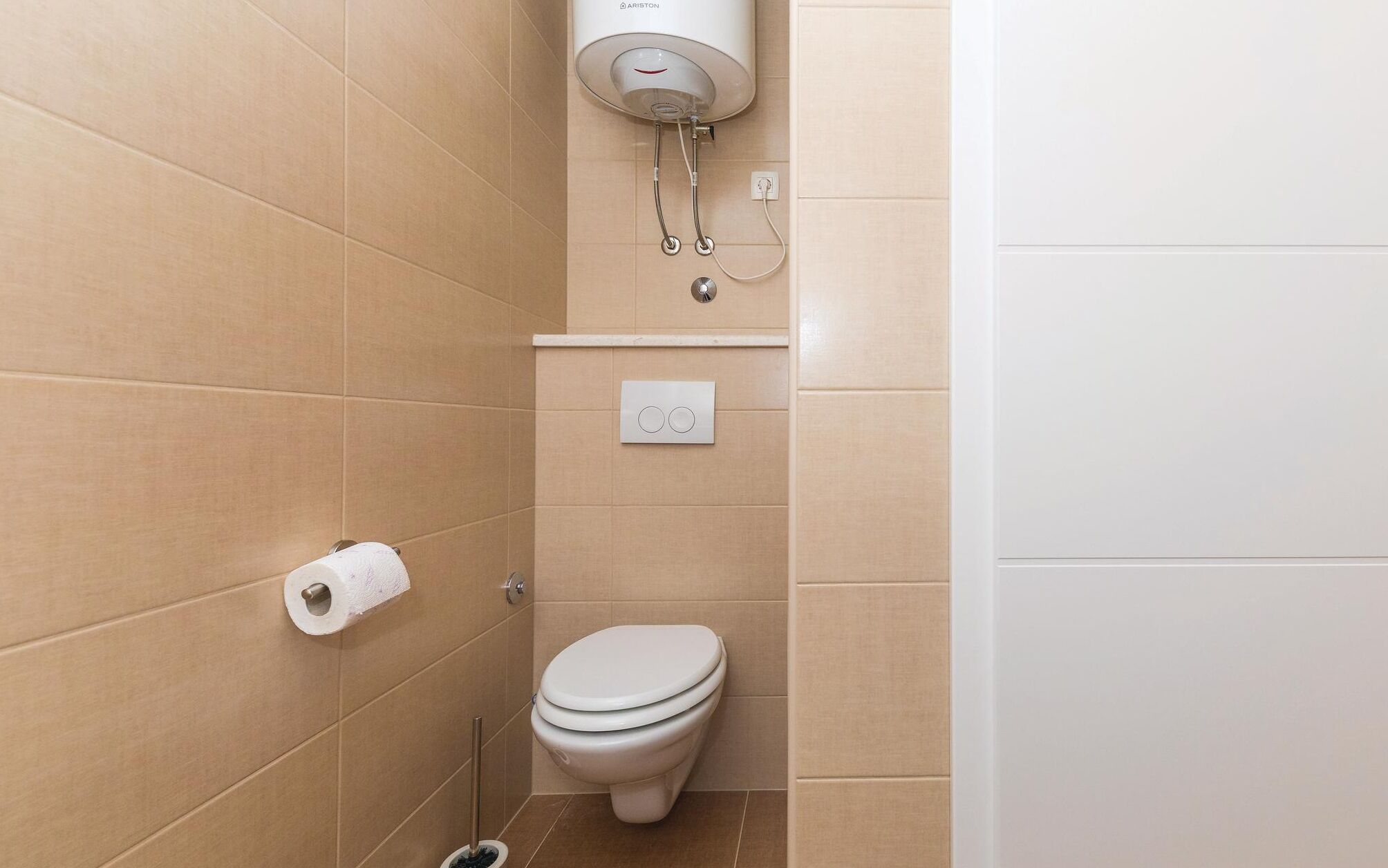 A small, clean bathroom with a toilet, a toilet paper holder, and a hand dryer mounted on the wall.
