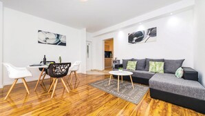 Una sala de estar moderna con un sofá gris, sillas blancas, una mesa de comedor con sillas y piso de madera.