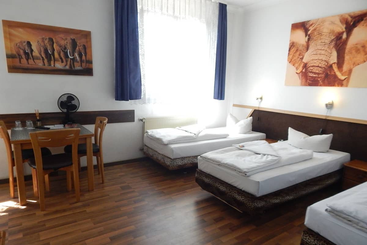 A hotel room with two beds, a dining table with chairs, a desk, and a window with curtains.