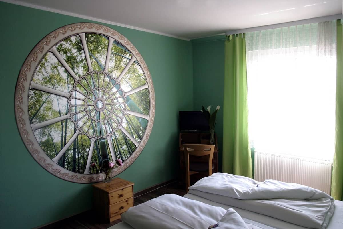 A room with a large circular mirror, a bed with white bedding, a wooden dresser, and a television on a stand.