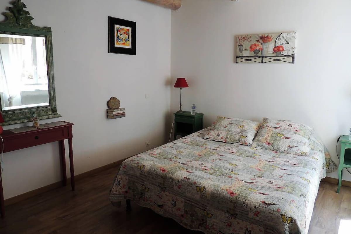 A bedroom with a bed, a nightstand, a dresser, a mirror, and two wall-mounted artworks.