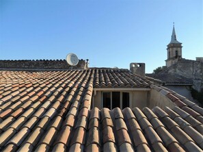 A rooftop with terracotta tiles, a satellite dish, and a church steeple in the background. - Eden Roque (La Roque-d'Antheron)