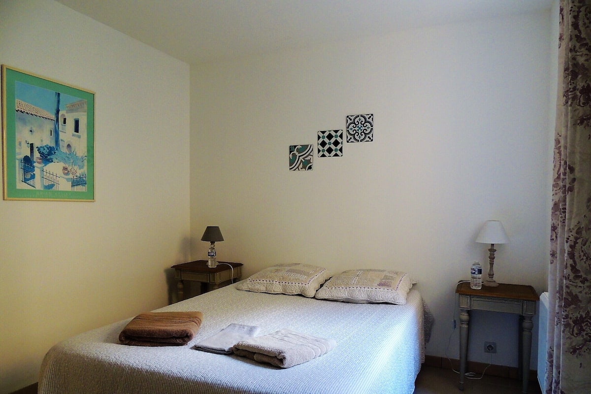 A neatly made bed with pillows and folded towels, a small bedside table with a lamp, and a wall with three decorative tiles.