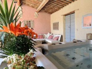 A spa area with a hot tub, a sofa, and a potted plant with orange flowers. - Eden Roque (La Roque-d'Antheron)