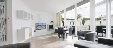 Uma sala de estar moderna com área de jantar, grandes janelas e vista para o exterior.