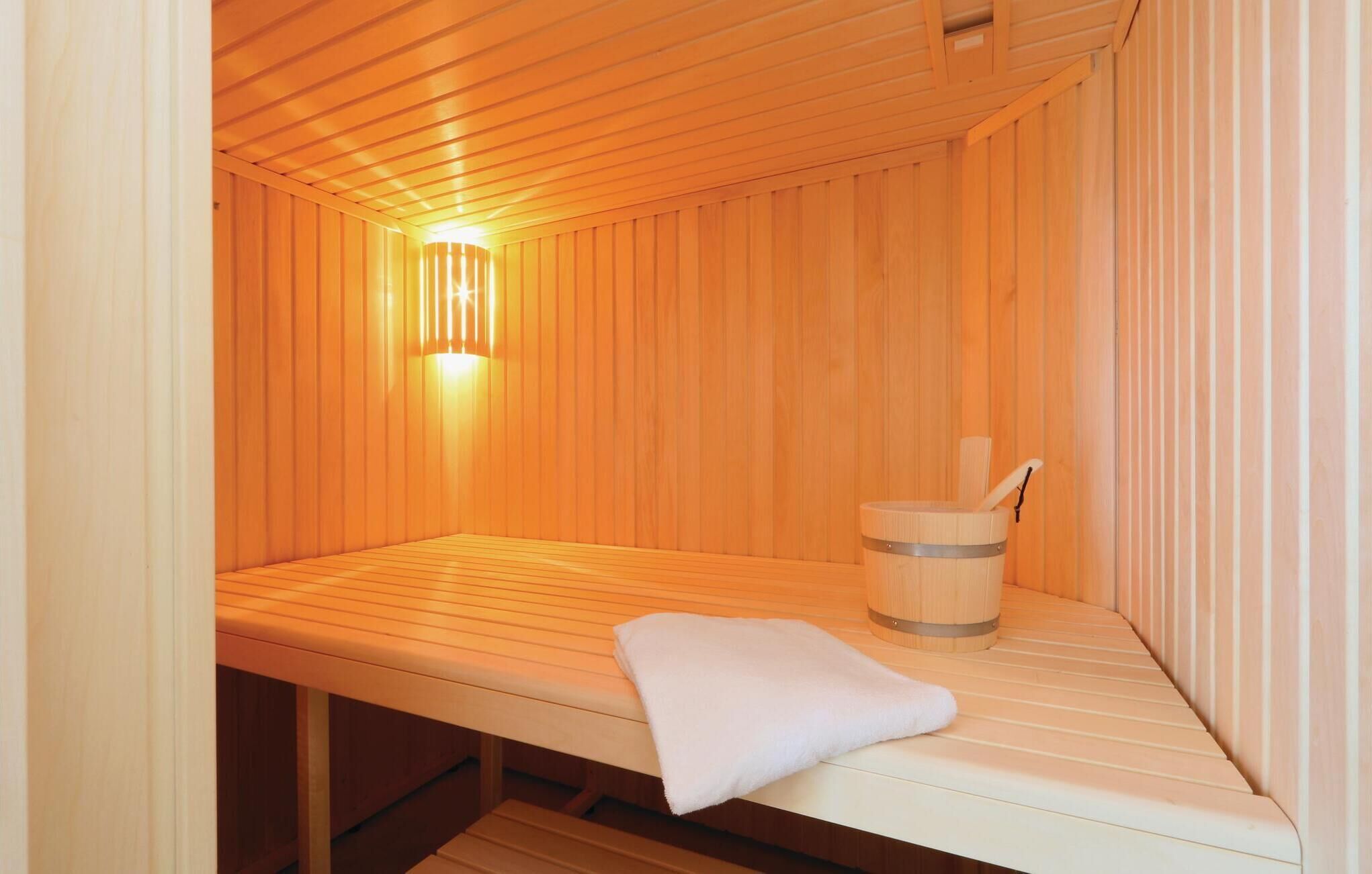 A sauna room with wooden walls, a bench, a towel, and a wooden bucket.