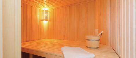 A sauna room with wooden walls, a bench, a towel, and a wooden bucket.