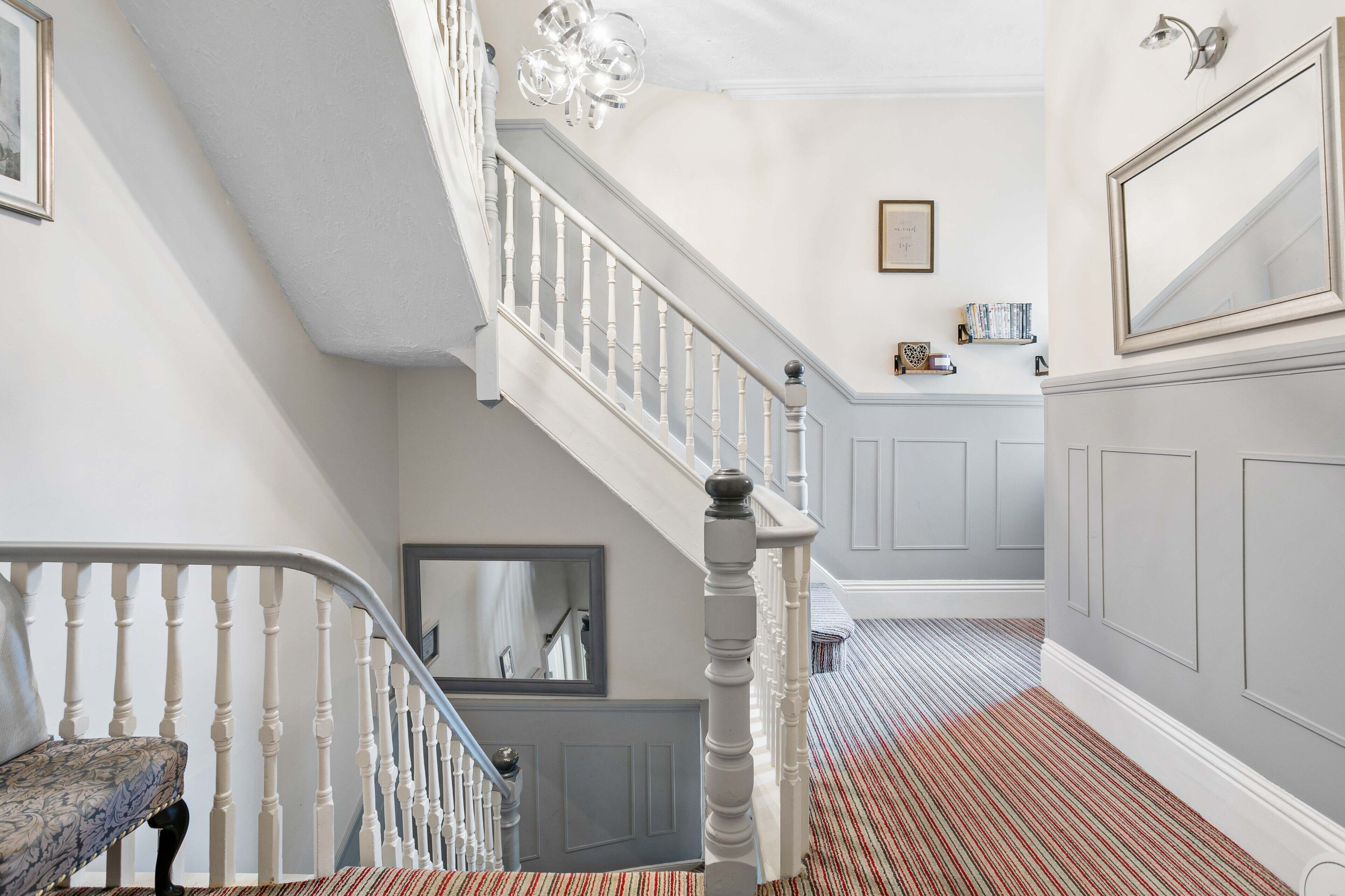 A staircase with white balusters, a patterned bench, and a striped carpet.