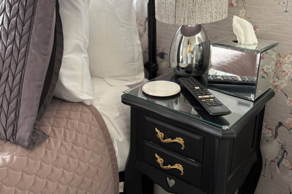 Un lit bien fait, avec un oreiller matelassé, une table de chevet sur laquelle se trouvent une boîte de mouchoirs, une télécommande et une lampe.