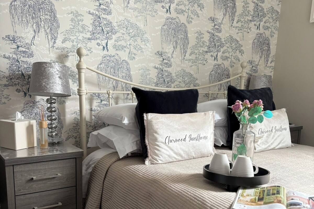Une chambre à coucher bien rangée, avec un lit, une table de chevet, une lampe et un coussin décoratif orné d’un motif textuel.