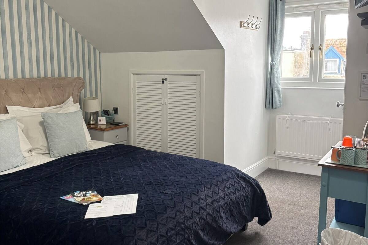 Une chambre à coucher comprenant un lit, une table de chevet, une commode, une fenêtre avec des rideaux et un radiateur.