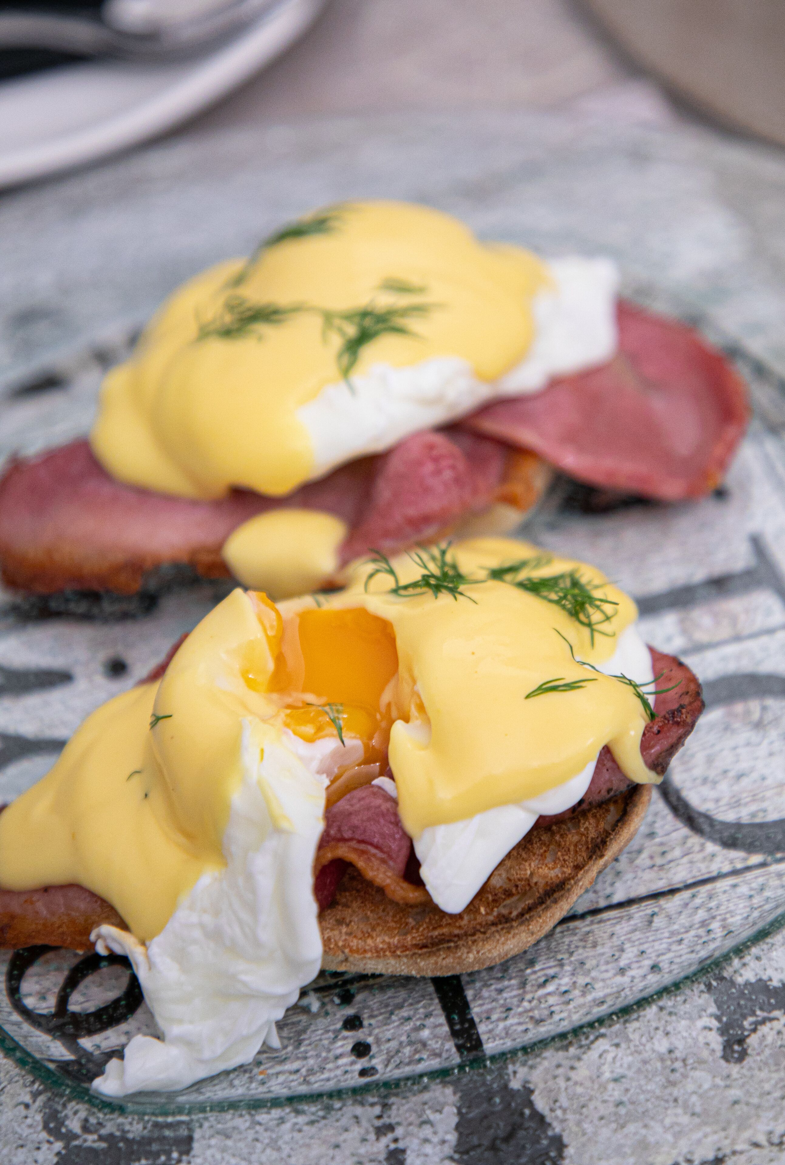 Un plat du petit-déjeuner composé d’œufs, de jambon et de sauce hollandaise, servi dans une assiette.