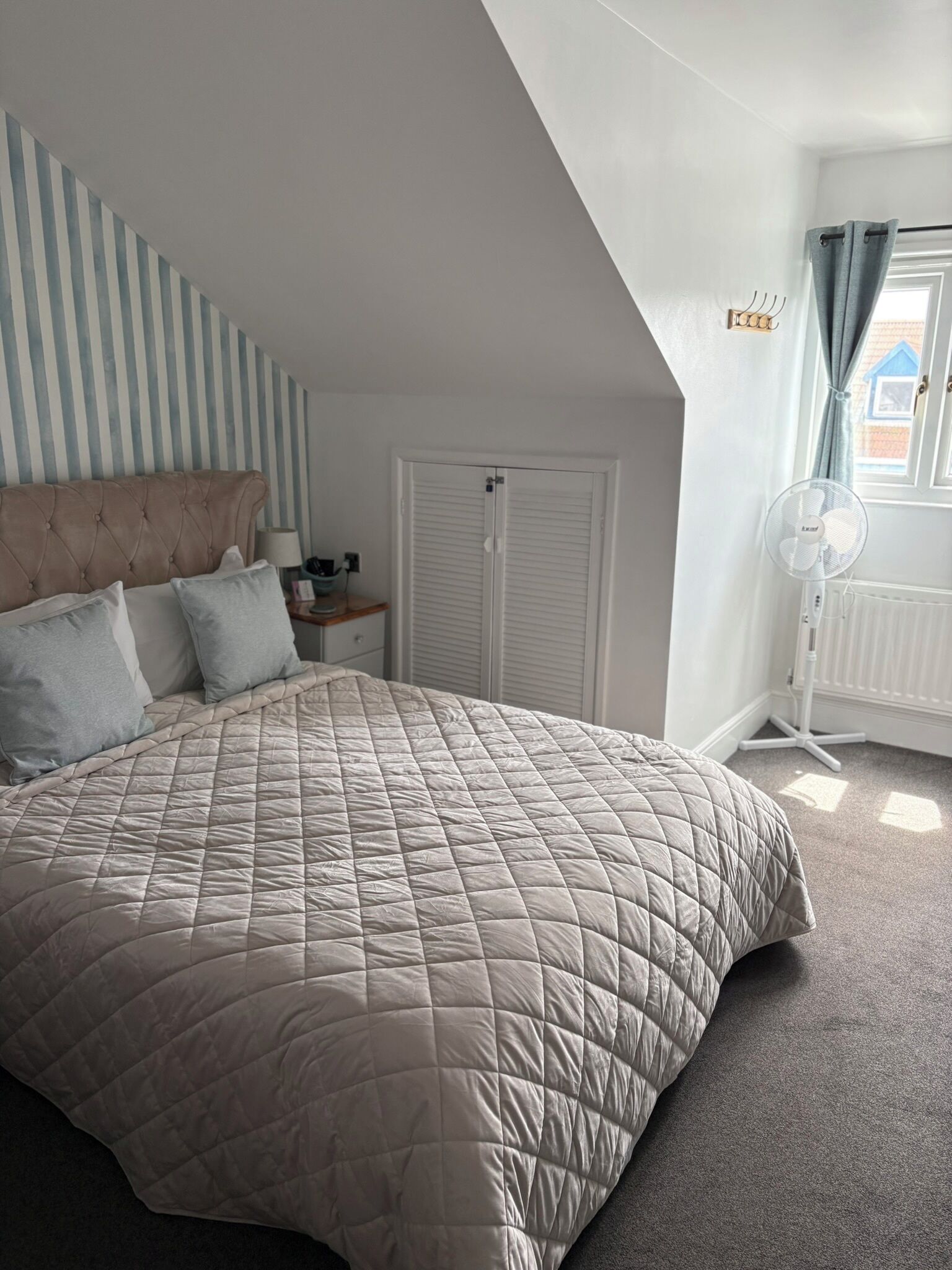 A bedroom with a large bed, a bedside table, a lamp, a window with curtains, and a radiator.