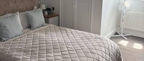 A bedroom with a large bed, a bedside table, a lamp, a window with curtains, and a radiator.