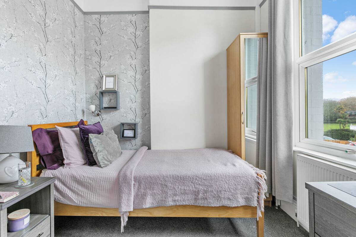 Une chambre à coucher avec un lit, une table de chevet, une lampe et une vue sur l’extérieur par une fenêtre.